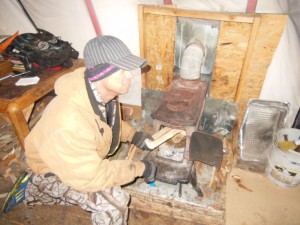Angelo putting wood into stove to warm tent